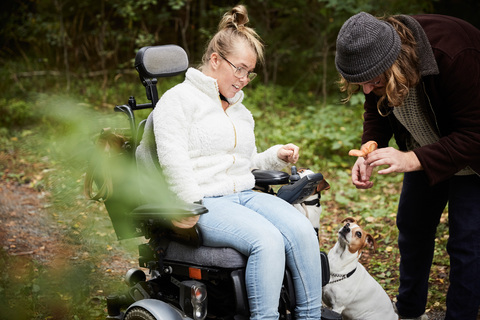 Behinderte Frau im Rollstuhl sieht Hausmeister an, der einen Pilz im Wald hält, lizenzfreies Stockfoto