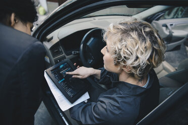 Ein weiblicher Mechaniker erklärt einem Kunden etwas über ein digitales Tablet, während er im Auto sitzt - MASF01886