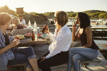 Freunde genießen das Mittagessen am Picknicktisch auf dem Steg im Sommer - MASF01906