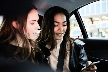 Freundinnen benutzen ihr Handy während der Fahrt im Taxi in der Stadt - MASF01928