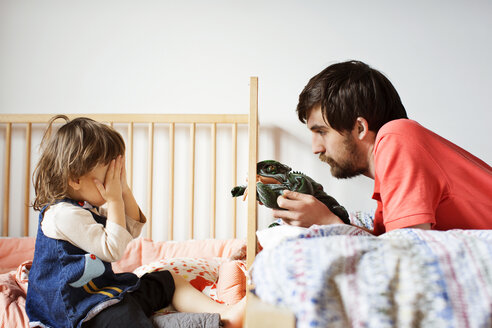 Vater und Tochter spielen mit Spielzeug am Bett im Haus - CAVF35388