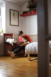 Vater und Tochter lesen ein Buch, während sie mit ihrem Hund zu Hause sitzen - CAVF35390