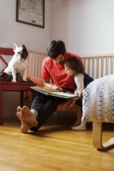 Vater und Tochter schauen sich ein Buch an, während sie mit ihrem Hund zu Hause sitzen - CAVF35391