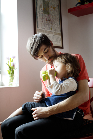 Vater schaut auf ein trinkendes Mädchen, das am Fenster sitzt, lizenzfreies Stockfoto