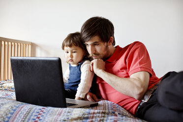 Vater und Tochter schauen auf einen Laptop, während sie sich auf dem Bett entspannen - CAVF35395