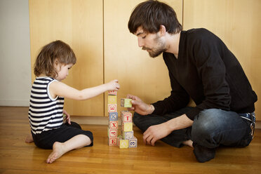 Vater und Tochter spielen mit Spielzeugblöcken, während sie zu Hause auf dem Boden sitzen - CAVF35397