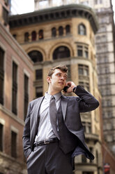 Businessman talking on smart phone while standing against buildings in city - CAVF35401