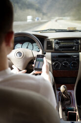 Rückansicht eines Mannes, der sein Smartphone während der Fahrt im Auto benutzt - CAVF35412