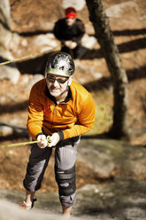 High angle view of man rappelling on rock face - CAVF35428