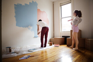 Woman hand on hip looking at man painting on wall - CAVF35437