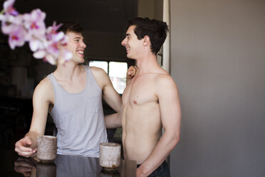Lächelndes homosexuelles Paar an der Küchentheke zu Hause - CAVF35442