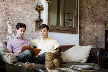 Gay men looking record while sitting on sofa at home - CAVF35455