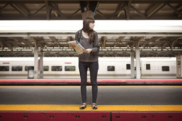 Frau mit Karte, die auf dem Bahnhof auf einen Zug wartet - CAVF35480