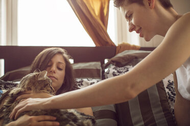 Women looking at cat while relaxing on bed at home - CAVF35492