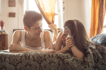Lesbians looking at each other while relaxing on bed at home - CAVF35499