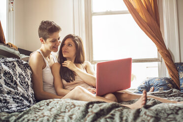 Lesben benutzen einen Laptop, während sie zu Hause auf dem Bett sitzen - CAVF35502