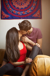 Zärtliches lesbisches Paar, das sich küsst, während es auf dem Sofa zu Hause sitzt - CAVF35510