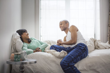 Smiling couple talking while relaxing on bed at home - CAVF35527