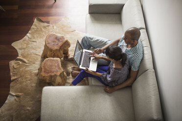 Blick von oben auf ein Paar, das einen Laptop benutzt, während es zu Hause auf dem Sofa sitzt - CAVF35535