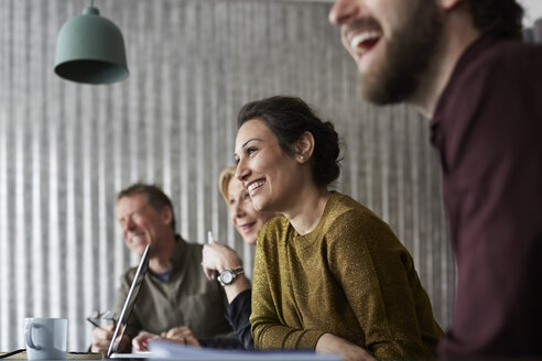 Fröhliche kreative Geschäftskollegen, die am Konferenztisch sitzen und im Sitzungssaal wegschauen - MASF01931