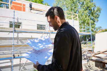 Businessman reading blueprints while standing at construction site on sunny day - MASF01932