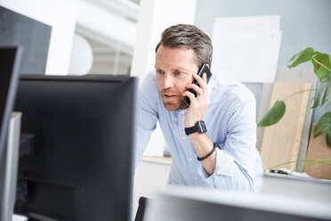 Geschäftsmann, der mit einem Mobiltelefon spricht, während er einen Computer am Schreibtisch im Büro benutzt - MASF01935