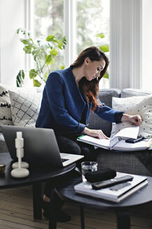 Geschäftsfrau liest ein Dokument, während sie auf dem Sofa im Heimbüro sitzt - MASF01945
