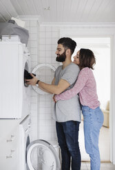 Woman embracing man while loading clothes in washing machine at home - MASF01956