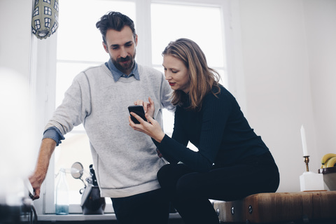 Junge Frau, die einem Mann am Fenster ihr Mobiltelefon zeigt, lizenzfreies Stockfoto