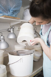 Junge Töpferin gießt Ton aus einer Vase in ein Sieb über einem Eimer in einer Werkstatt - MASF01990