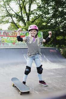 Lächelndes Mädchen, das Muskeln anspannt, während es auf einer Skateboard-Rampe steht - MASF02006
