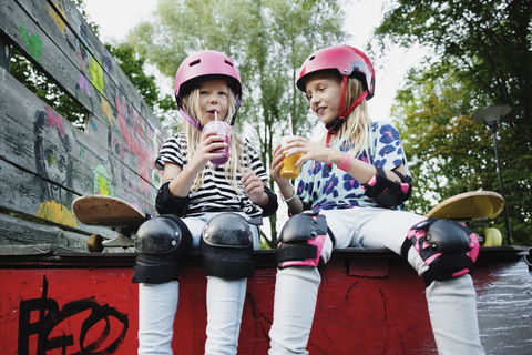 Lächelnde Freunde genießen ein Getränk, während sie auf dem Rand einer Skateboard-Rampe sitzen, lizenzfreies Stockfoto