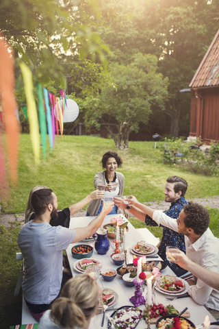 Lächelnde Frau stößt mit Freunden an einem Tisch in einem Gartenfest an, lizenzfreies Stockfoto