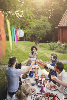 Lächelnde Frau stößt mit Freunden an einem Tisch in einem Gartenfest an - MASF02015