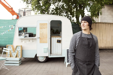 Nachdenklicher männlicher Besitzer, der wegschaut, während er vor einem Imbisswagen auf der Straße steht, lizenzfreies Stockfoto