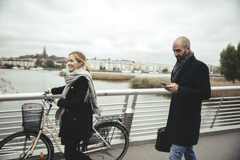 Lächelnde Geschäftsfrau mit Fahrrad geht an Geschäftsmann auf Brücke vorbei - MASF02027