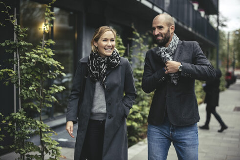 Lächelnder Geschäftsmann und Geschäftsfrau unterhalten sich beim Gehen auf dem Bürgersteig - MASF02029