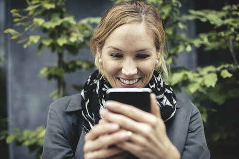 Lächelnde Geschäftsfrau im mittleren Erwachsenenalter, die ein Smartphone im Freien benutzt - MASF02030