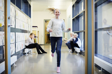 Smiling girl running in school corridor with friends in background - MASF02044