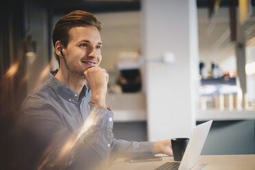 Thoughtful businessman sitting with hand on chin at desk in office - MASF02053