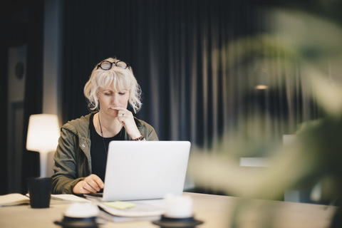 Nachdenkliche Geschäftsfrau mit Laptop am Schreibtisch im Büro, lizenzfreies Stockfoto