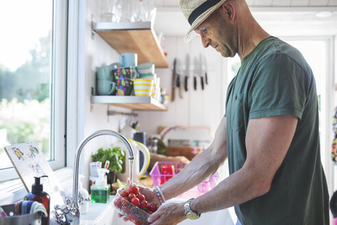 Side view of man washing cherry tomatoes under faucet in kitchen at home - MASF02059