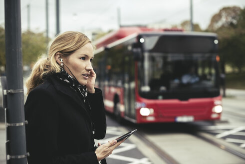 Seitenansicht einer Geschäftsfrau, die mit einem Mobiltelefon spricht, mit einem Bus im Hintergrund - MASF02070