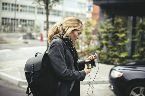 Side view of mid adult businesswoman holding smart phone while walking on city street stock photo
