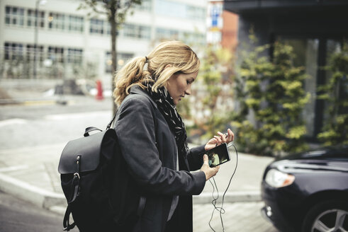 Seitenansicht der mittleren erwachsenen Geschäftsfrau, die ein Smartphone hält, während sie auf der Straße geht - MASF02071
