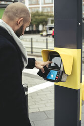 Seitenansicht eines Geschäftsmannes, der einen Fahrkartenscanner auf einem Bürgersteig in der Stadt bedient - MASF02073