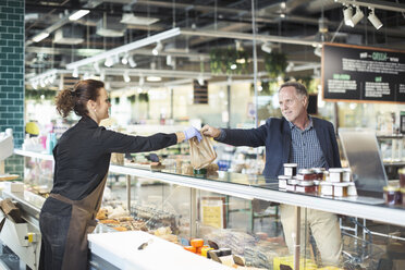 Seitenansicht einer Verkäuferin, die einem reifen Mann im Bio-Supermarkt ein Paket überreicht - MASF02076