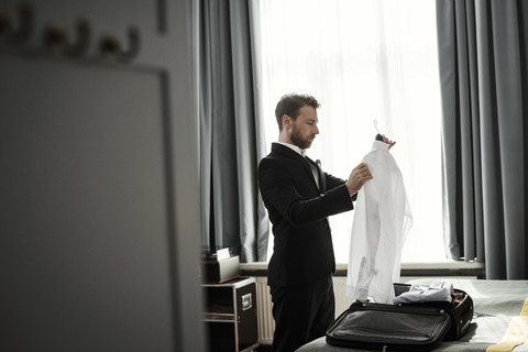 Seitenansicht eines Geschäftsmannes, der ein weißes Hemd in einem Kleiderbügel in einem Hotelzimmer hält, lizenzfreies Stockfoto