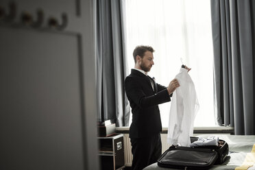 Seitenansicht eines Geschäftsmannes, der ein weißes Hemd in einem Kleiderbügel in einem Hotelzimmer hält - MASF02088