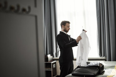 Side view of businessman holding white shirt in coathanger at hotel room - MASF02088
